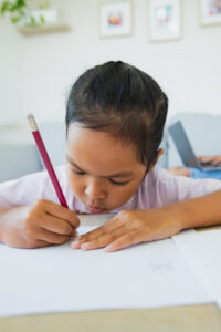 young girl writing on white paper with a pencil