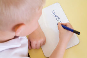 little boy writing his name on a small whiteboard
